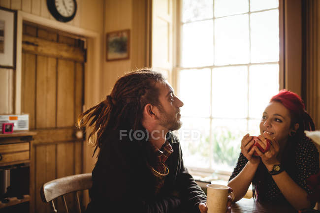 Casal sorrindo enquanto toma café na mesa em casa — Fotografia de Stock