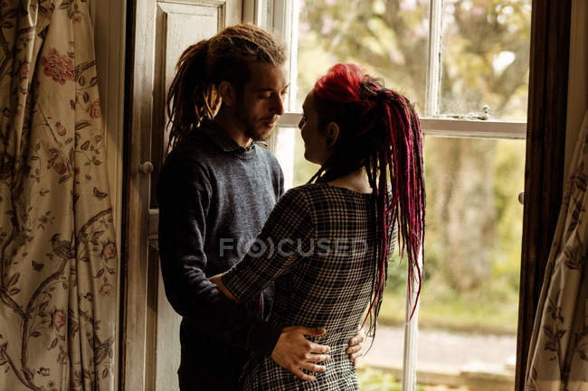 Jeune couple embrassant par la fenêtre à la maison — Photo de stock