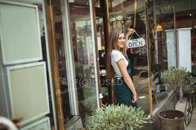 Fleuriste femelle tenant un panneau ouvert devant le magasin de fleurs — Photo de stock