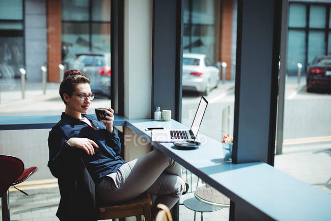 Jeune femme d'affaires tenant une tasse de café assis sur une chaise dans un café — Photo de stock