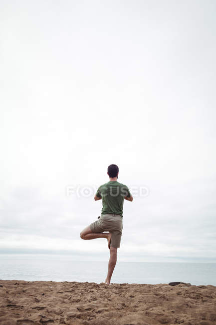 Vue arrière de l'homme effectuant du yoga sur la plage — Photo de stock
