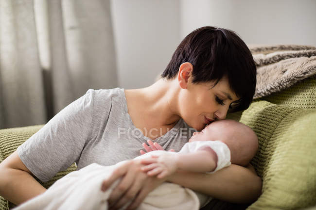 Mãe beijando a testa do bebê enquanto filho dormindo na sala de estar em casa — Fotografia de Stock