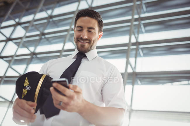Piloto con teléfono móvil en la sala de espera en la terminal del aeropuerto - foto de stock