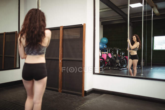 Back view of Pole dancer holding pole and looking at mirror in fitness studio — Stock Photo