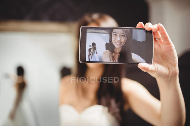 Mujer tomando selfie mientras se prueba el vestido de novia en el estudio - foto de stock