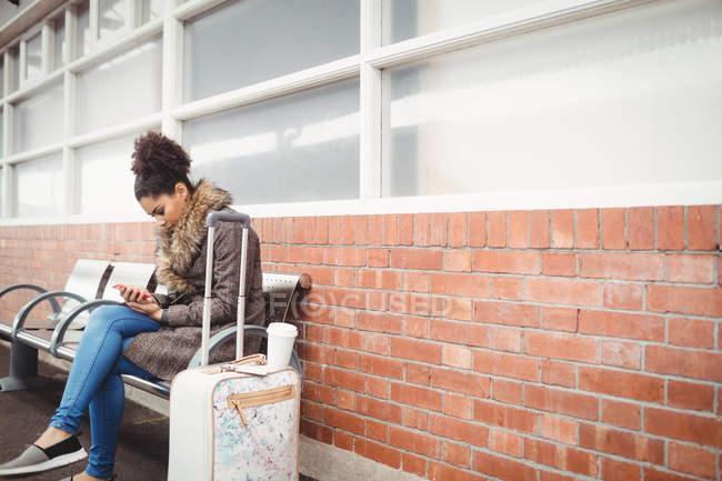 Молодая женщина использует телефон, сидя на железнодорожной станции платформы — стоковое фото