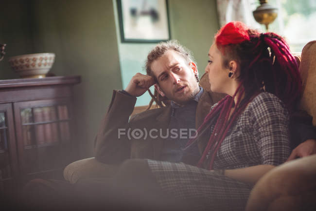 Casal jovem conversando enquanto sentado no sofá em casa — Fotografia de Stock