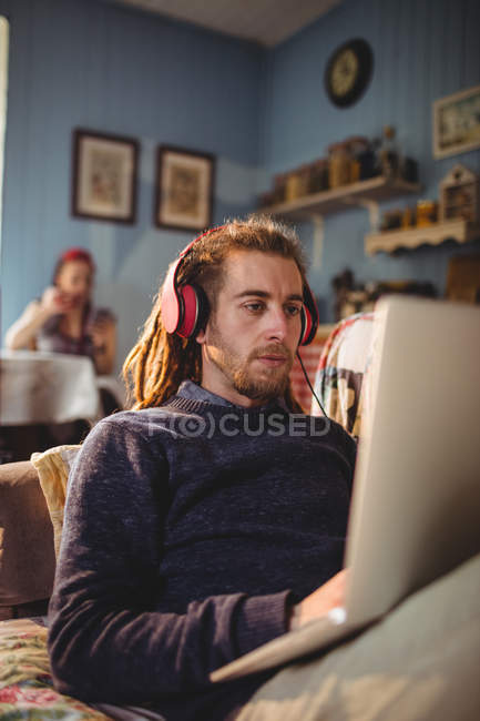 Hipster uomo utilizzando il computer portatile durante l'ascolto di musica a casa — Foto stock