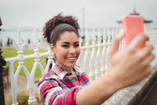 Sorridente donna prendere selfie mentre in piedi da ringhiera — Foto stock
