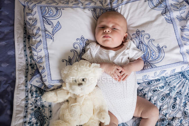 Младенец, спящий на кровати с плюшевым медведем дома — стоковое фото