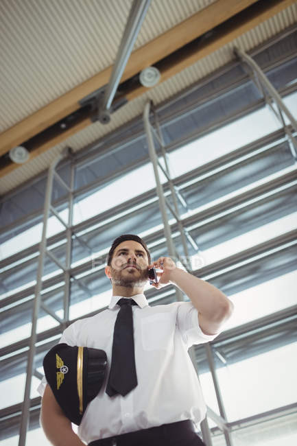 Пілот розмовляє по мобільному телефону в зоні очікування в терміналі аеропорту — стокове фото