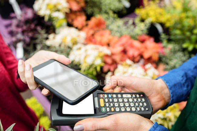 Abgeschnittenes Bild einer Frau, die im Blumenladen mit dem Smartphone bezahlt — Stockfoto
