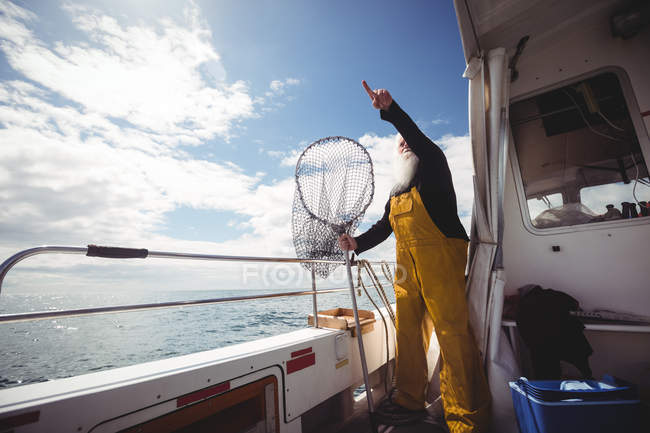 Fischer hält Fischernetz in der Hand und zeigt vom Boot auf den Himmel — Stockfoto