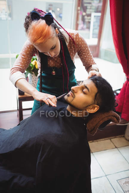 Al hombre le cortan la barba con tijera en la peluquería. - foto de stock