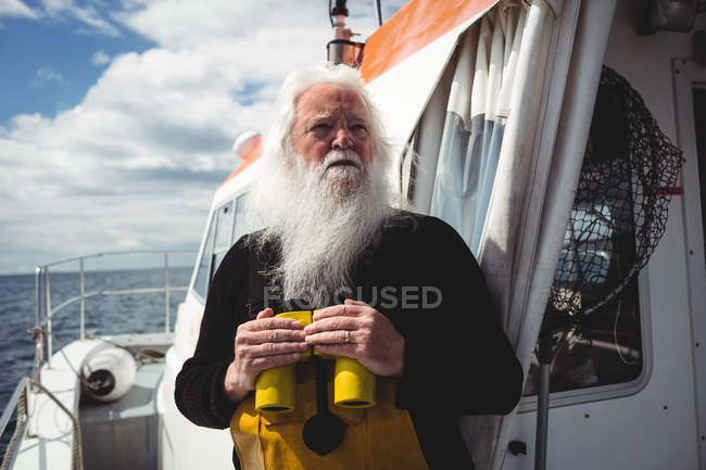 Fisherman holding binoculars and looking away from boat — Stock Photo