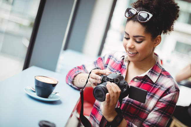 Mujer joven sonriente sosteniendo la cámara mientras está de pie en el restaurante - foto de stock
