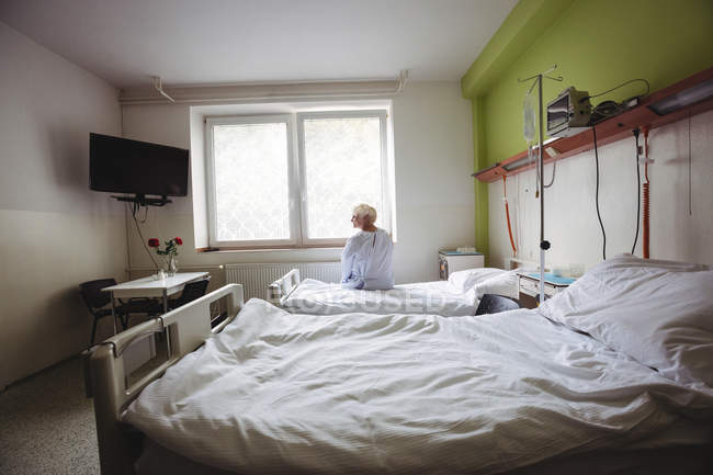 Senior woman sitting on bed in hospital ward — Stock Photo