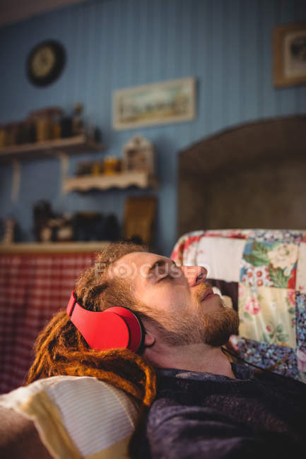 Jovem hipster homem ouvir música enquanto relaxa no sofá em casa — Fotografia de Stock
