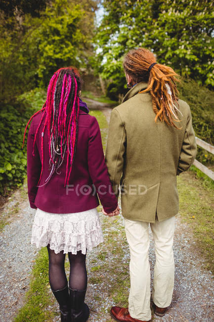 Rear view of hipster couple holding hands while standing in park — Stock Photo