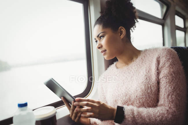 Frau schaut durch Fenster, während sie Tablet im Zug hält — Stockfoto