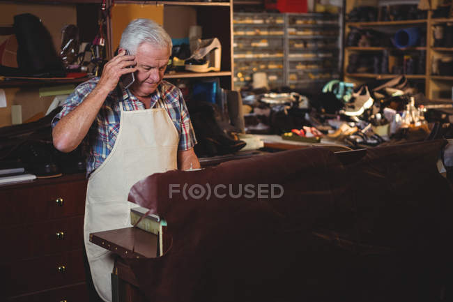 Senior shoemaker talking on the mobile phone in workshop — Stock Photo