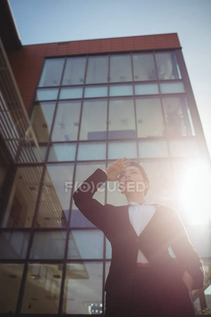 Low angle view of woman shielding eyes against office building — Stock Photo