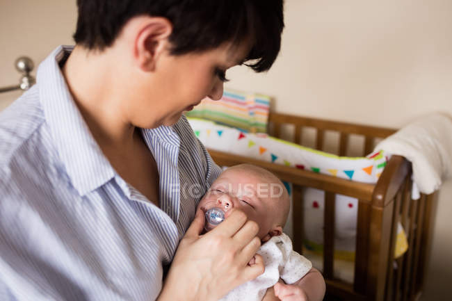Mãe colocando manequim na boca do bebê em casa — Fotografia de Stock