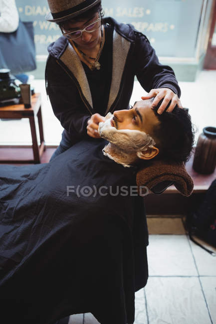 Man getting his beard shaved with shaving brush in barber shop — Stock Photo