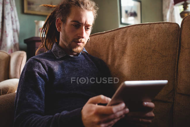 Молодий чоловік використовує цифровий планшет, сидячи на дивані вдома — стокове фото