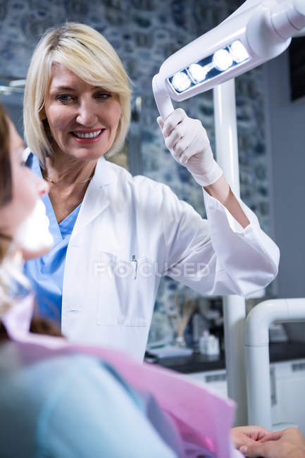 Dentiste souriant ajustant la lumière sur la bouche du patient à la clinique dentaire — Photo de stock
