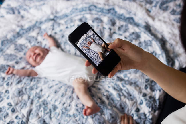Мама фотографирует своего ребенка со смартфоном в спальне дома — стоковое фото