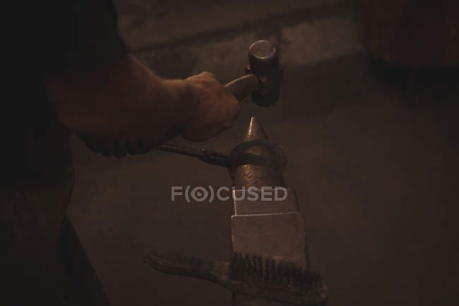 Close-up of blacksmith holding red hot metal horseshoe with tongs on anvil using hammer to shape — Stock Photo