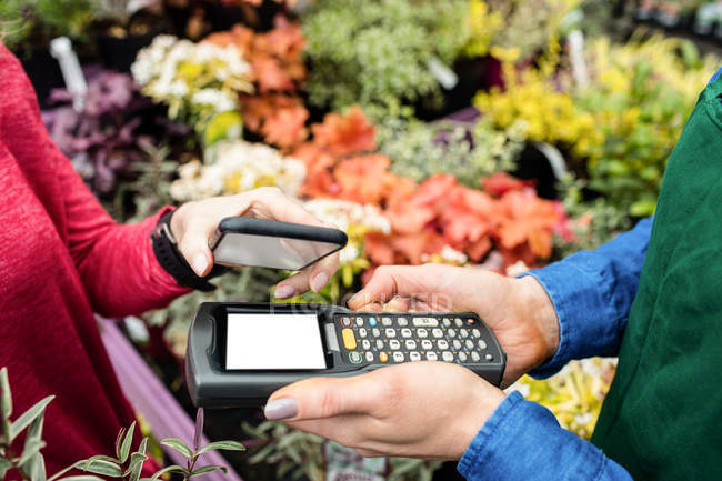 Imagen recortada de la mujer haciendo el pago a través de teléfono inteligente en la tienda de flores - foto de stock