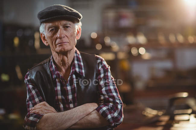 Portrait of shoemaker standing with arms crossed in workshop — Stock Photo