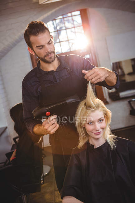 Portrait of smiling woman getting her hair dried with hair dryer at hair salon — Stock Photo