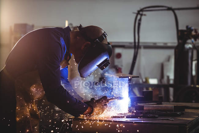Мужской сварщик работает на куске металла в мастерской — стоковое фото