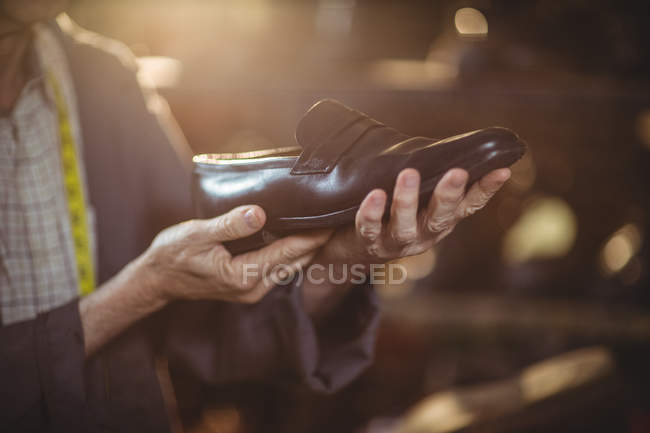 Sección media del zapatero examinando un zapato en el taller - foto de stock