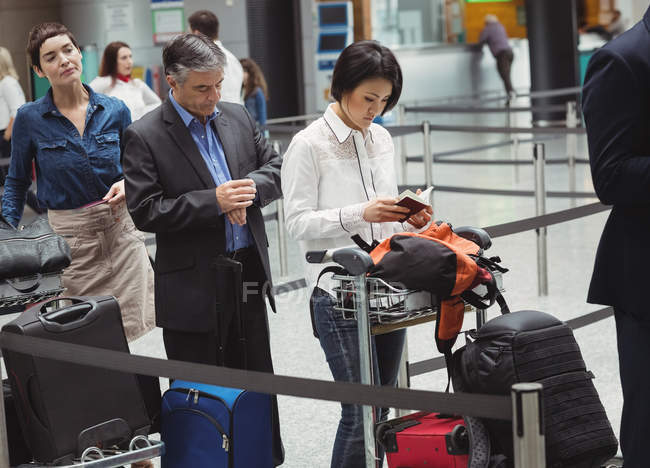 Пассажиры, стоящие в очереди у стойки регистрации с багажом внутри терминала аэропорта — стоковое фото