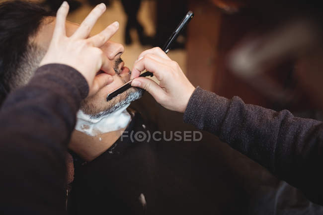 Uomo ottenere la barba rasata con rasoio in negozio di barbiere — Foto stock