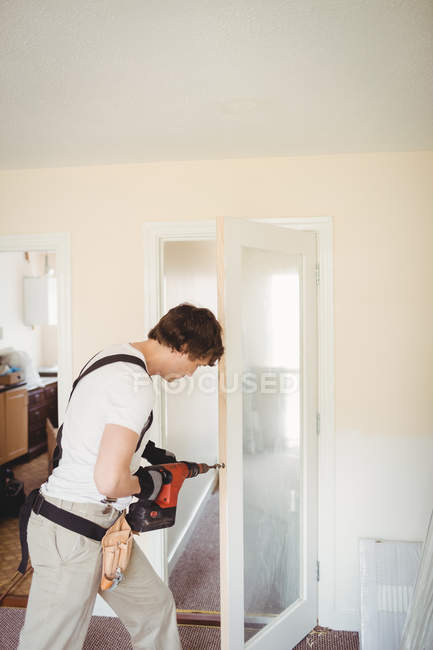 Carpintero perforando puerta de madera con máquina de perforación en casa - foto de stock