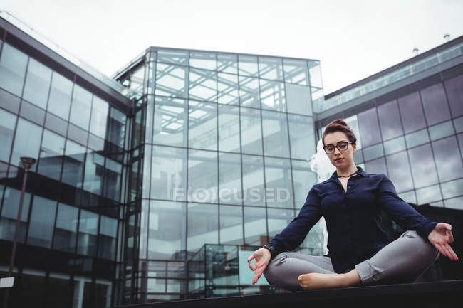 Konzentrierte Geschäftsfrau macht Yoga gegen das Bauen — Stockfoto