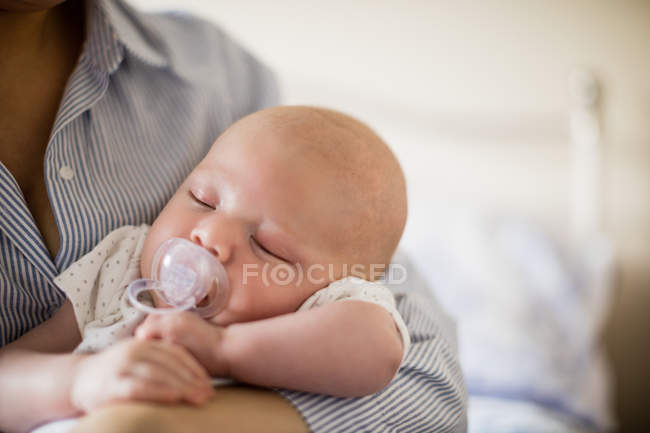 Cropped image of baby with dummy sleeping in mother arms at home — Stock Photo