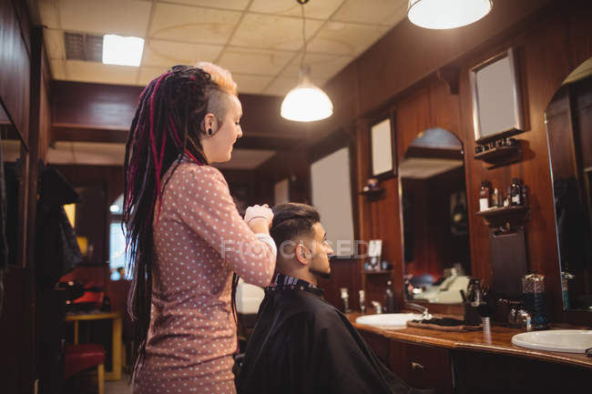 Female barber styling customer hair in barber shop — Stock Photo