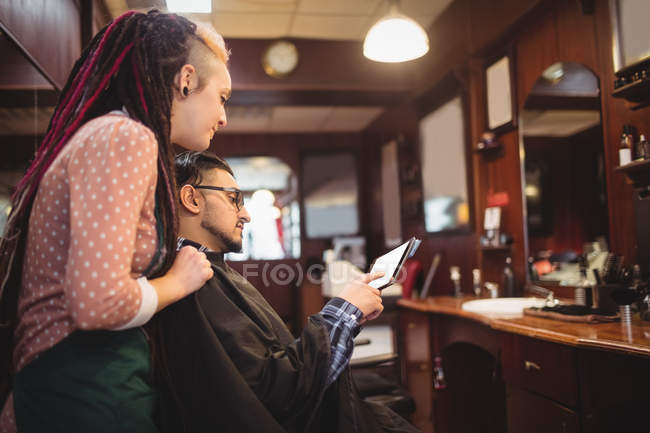 Cliente che mostra tablet digitale al barbiere donna nel negozio di barbiere — Foto stock
