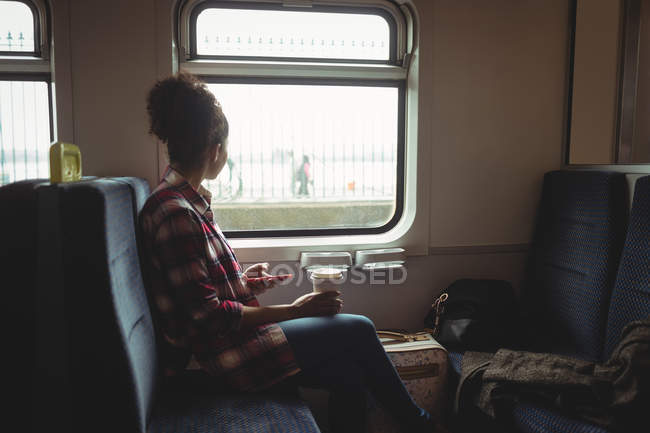 Женщина смотрит в окно, держа мобильный телефон в поезде — стоковое фото
