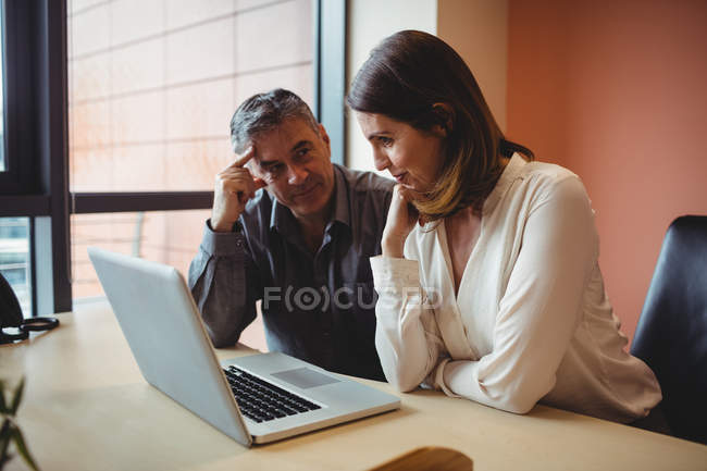 Hombre y mujer discutiendo sobre el ordenador portátil en la oficina - foto de stock