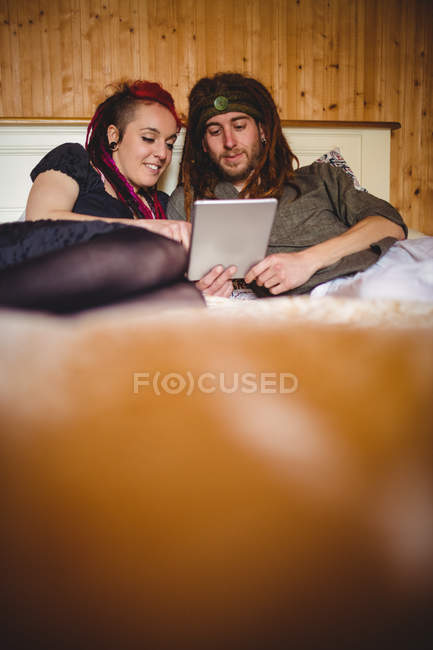 Casal Hipster usando tablet digital enquanto relaxa na cama em casa — Fotografia de Stock