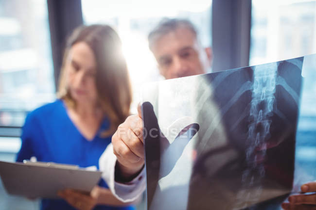 Врач осматривает рентген, пока медсестра пишет на планшете в больнице — стоковое фото