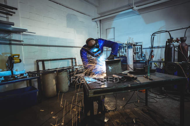 Мужской сварщик работает на куске металла в мастерской — стоковое фото