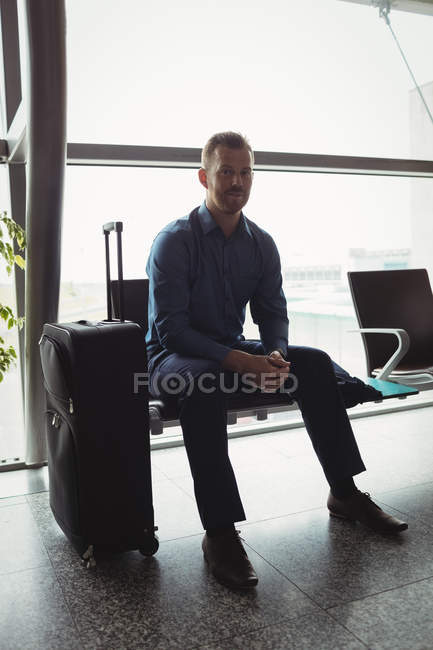 Businessman sitting with luggage at waiting area in airport terminal — Stock Photo